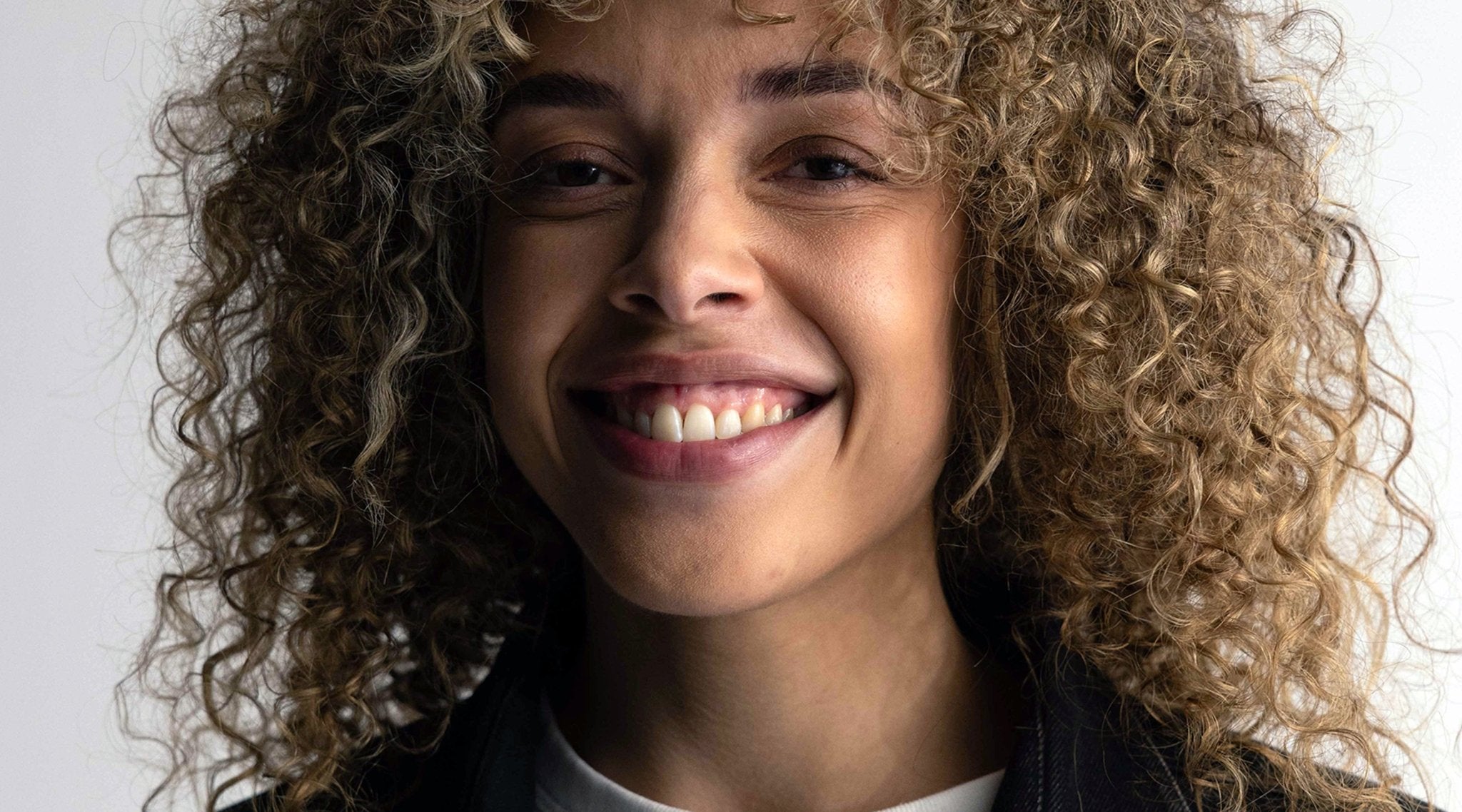 Frau mit Locken lacht, offener Mund und Zähne sind zu sehen.