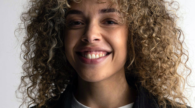 Frau mit Locken lacht, offener Mund und Zähne sind zu sehen.