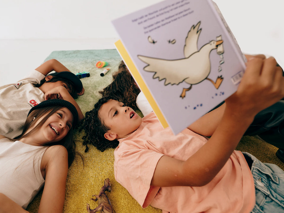 Kinder liegen auf dem Teppich und lesen das Buch